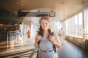 Theme tourism travel. Young beautiful Caucasian woman in dress and hat with backpack tourist mat in terminal station in a long