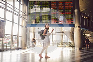 Theme travel and tranosport. Beautiful young caucasian woman in dress and backpack standing inside train station or terminal looki photo