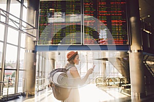 Theme travel and tranosport. Beautiful young caucasian woman in dress and backpack standing inside train station or terminal looki