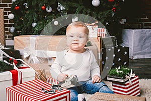 Theme winter and Christmas holidays. Child boy Caucasian blond 1 year old sitting home floor near Christmas tree with New Year dec