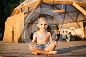Theme is yoga and children. Caucasian Boy child sitting barefoot cross-legged in lotus position on wooden floor the