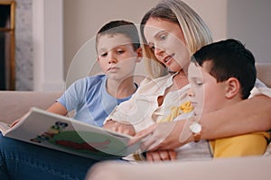 And then he ate the kids because they wouldnt sleep. Shot of a mother reading a book to her sons at home on the couch.