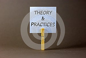 Theory and practice symbol. White paper with words `Theory and practice`, clip on wooden clothespin. Beautiful grey background.