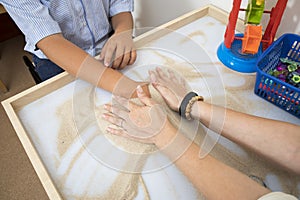 Therapeutic activities with children. A doctor helps a patient with autism play with sand