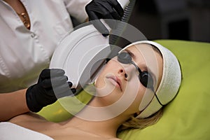 Therapist beautician makes a laser treatment to young woman`s fa