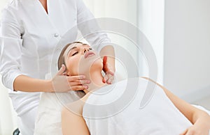 Therapist doing myofascial or buccal massage on face and head for female client lying at beauty center or spa salon