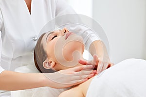 Therapist doing myofascial or buccal massage on face and head for female client lying at beauty center or spa salon