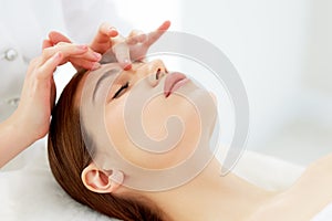 Therapist doing myofascial or buccal massage on face and head for female client lying at beauty center or spa salon