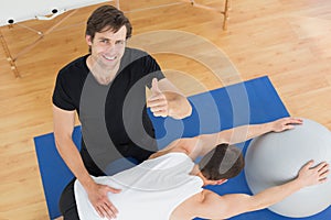 Therapist gesturing thumbs up by man with yoga ball