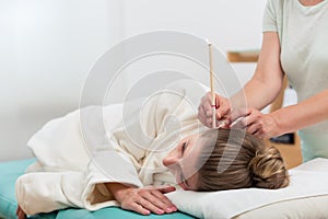 Therapist hand with burning ear candle in woman`s ear