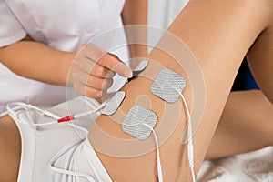 Therapist placing electrodes on woman's thigh