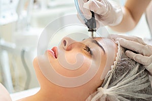 Therapist& x27;s hands holding hydrafacial tool and performing anti aging progress to young woman forehead at beauty