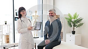 Therapist with tablet posing in doctor's office with patient