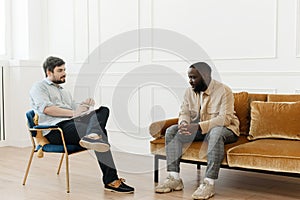 The therapist takes notes while talking to a depressed male patient and talks to an African American patient. Desperate