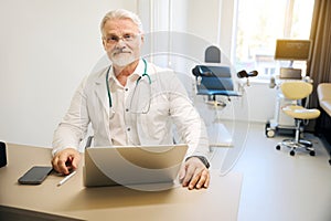 Therapist in white coat sitting at laptop in clinical office