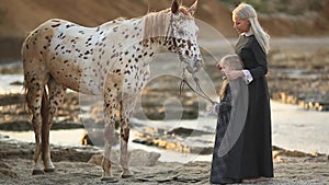 Therapy with horses - hippo therapy. Woman with daughter and mottled horse