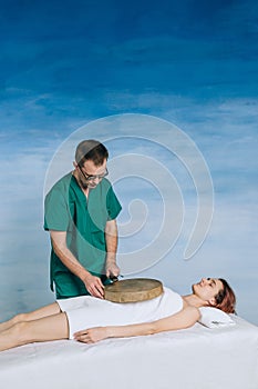 The therapy of a woman with a tambourine. Male masseur does nontraditional methods of medicine. Beautiful relaxed face