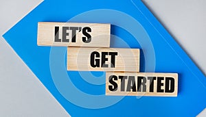 There is a blue notebook on a light gray background. Above are three wooden blocks with the words LET IS GET STARTED