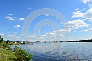 There is a boat on the river. River port. Bridge. Forest. Nature. Sunny weather. The sky, clouds scatter