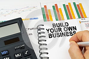 There is a calculator on the table, business charts, a man made a note in a notebook - Build Your Own Business
