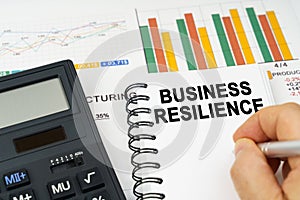 There is a calculator on the table, business charts, a man made a note in a notebook - business resilience