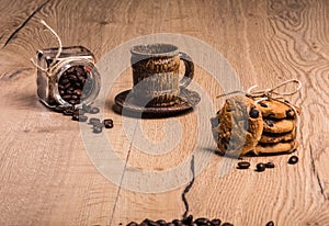 There is a coffee cup with a saucer made of coconut palm wood. From glass jar chaotically scattered roasted coffee beans