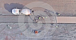 There is a concrete mixer truck that is pouring cement over sidewalk workers while the construction is underway