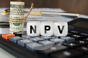 There are cubes on the calculator that say - NPV. Nearby out of focus - dollars, notebook and pen