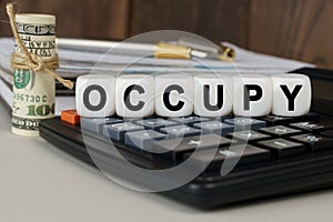 There are cubes on the calculator that say - OCCUPY. Nearby out of focus - dollars, notebook and pen