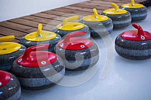 There are curling stones with red and yellow handles on the ice. The stones are ready to play