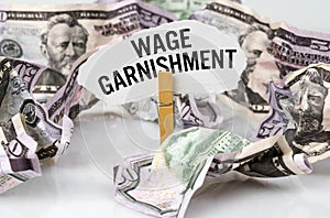 There are dollars on the table and there is a clothespin with paper on which it is written - WAGE GARNISHMENT