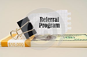 There are dollars on the table, on which there is a clip and torn paper with the inscription - Referral Program