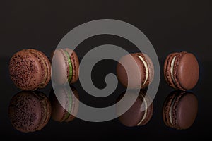 There are four chocolate cocoa flavored macarons on the black table