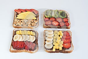 There are four sandwiches on the white surface. Bread covered with chocolate paste, strawberry and banana, mango. A sweet