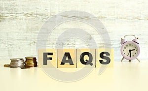 There are four wooden cubes with letters on the table next to the coins. FAQS word. On a gray background.