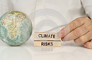 There is a globe on a white reflective surface, in the hands of wooden blocks with the inscription - Climate risks photo