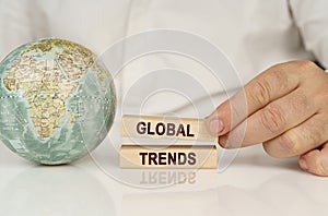 There is a globe on a white reflective surface, in the hands of wooden blocks with the inscription - GLOBAL TRENDS photo