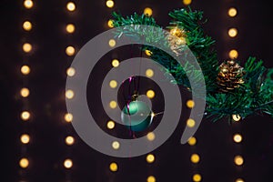 There is green ball on the green xmas tree branch. There are glowing lights/bokeh and on the background.