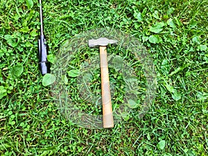 There is a hammer and a screwdriver on the grass. tools for repairs are laid out on the lawn. hammer on a wooden handle with a