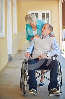 There for him when he needs it most. a senior woman pushing her husband in a wheelchair at a retirement home.