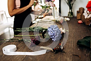 There are hydrangea, carnation and other flowers, scissors and ribbon on the table in flower shop