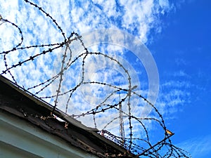 Iron fence gray. On top of wound barbed wire with spikes. Against a blue sky with clouds