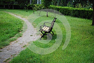 There is a leisure bench on the green grass beside the path in the park