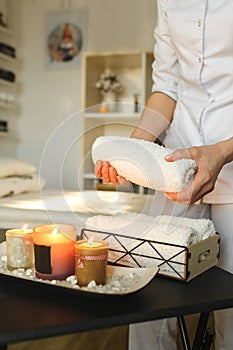 There are lit aromatic candles on the table, a spa center employee puts towels for treatments