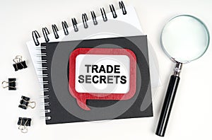 There is a magnifying glass, a notebook and a sign on the table - TRADE SECRETS