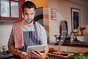 There are so many recipes I havent tried yet. Shot of a happy young man using his tablet while cooking in his kitchen at
