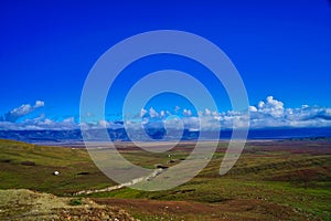 There is a meandering river in the yellow-green grass. A mountain range