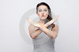 There is no way. Portrait of serious beautiful young brunette woman with makeup and striped dress standing with crossed hands and