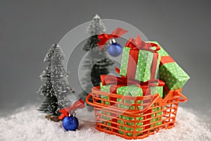 There is an orange shopping basket on the snow. The basket contains gifts in bright packaging with a red bow