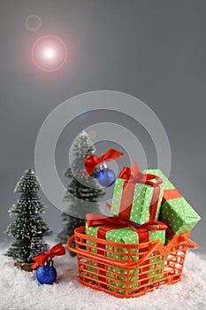 There is an orange shopping basket on the snow. The basket contains gifts in bright packaging with a red bow